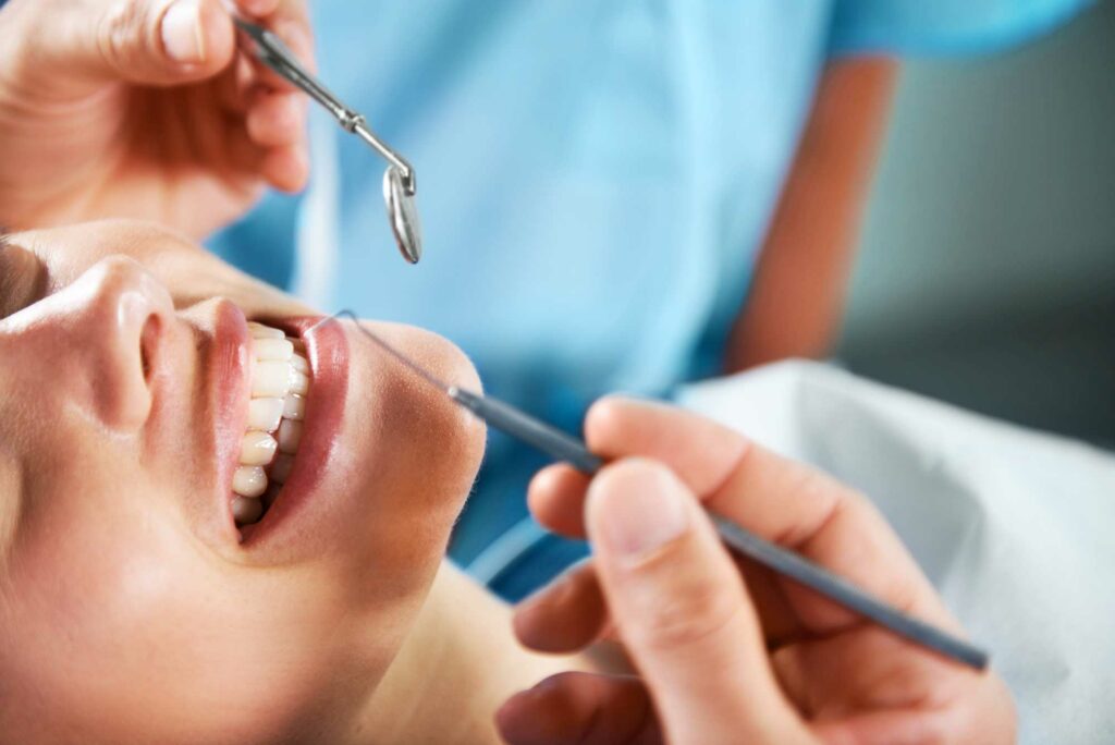 woman smiling at the dentist office as a dental professional holds dental tools